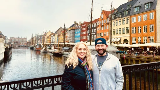 a man and woman pose for a photo on a bridge with a canal in the background