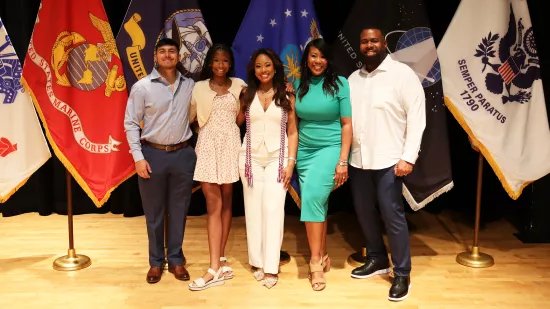 Five people pose for a photo in front of a group of flags.