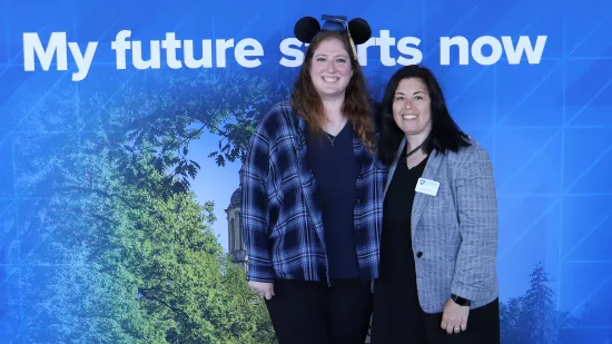 Two women stand in front of a Penn State photo background.