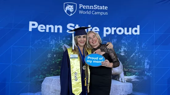 Two women pose in front of a Penn State photo background.