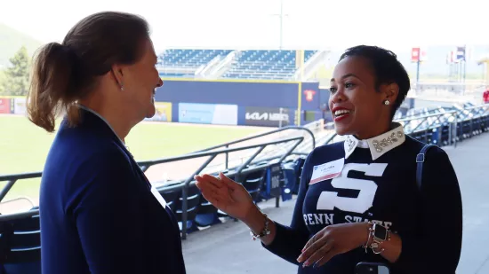 Two women talk in a baseball stadium.
