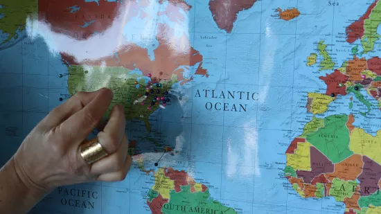 A hand pushes a pin into a world map with other pins.