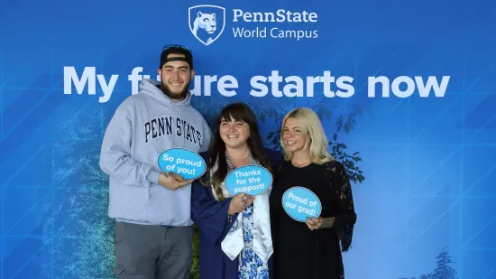Three people hold signs in front of a Penn State photo background.