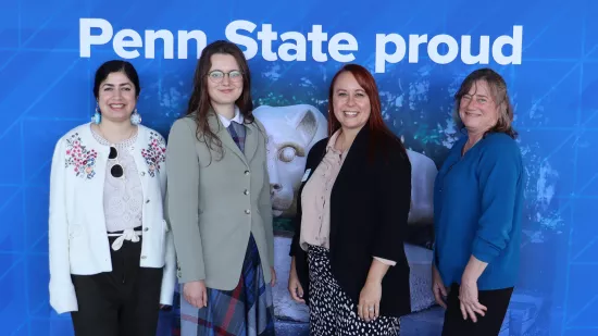 Four people pose in front of a Penn State background.