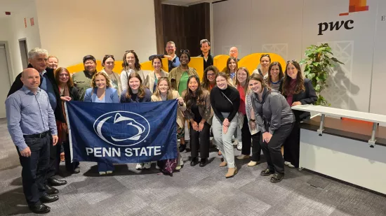 A group of people hold a Penn State flag in an office lobby area.