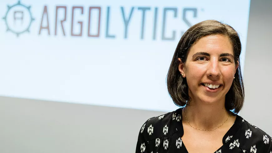 Tamela Serensits is standing in front of a projector with her company's name, Argolytics, showing.