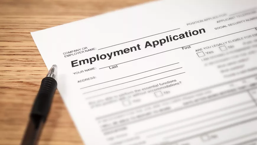 An employment application is shown with a pen on a wooden surface