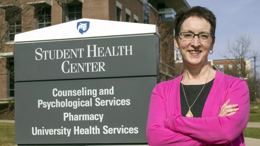 Shelley Haffner stands in front of a sign that says Student Health Center, which is in front of the University Health Services building on Penn State's campus