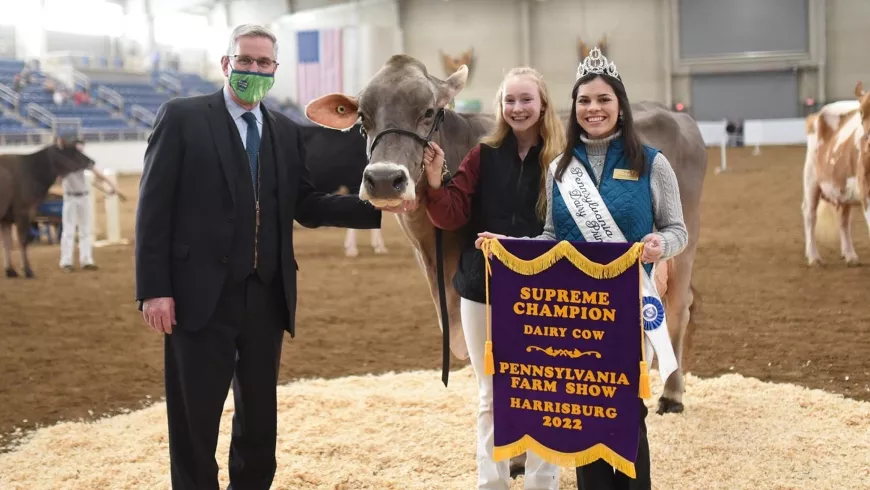 Mikayla Davis stands next to two other people and a dairy cow in show ring.