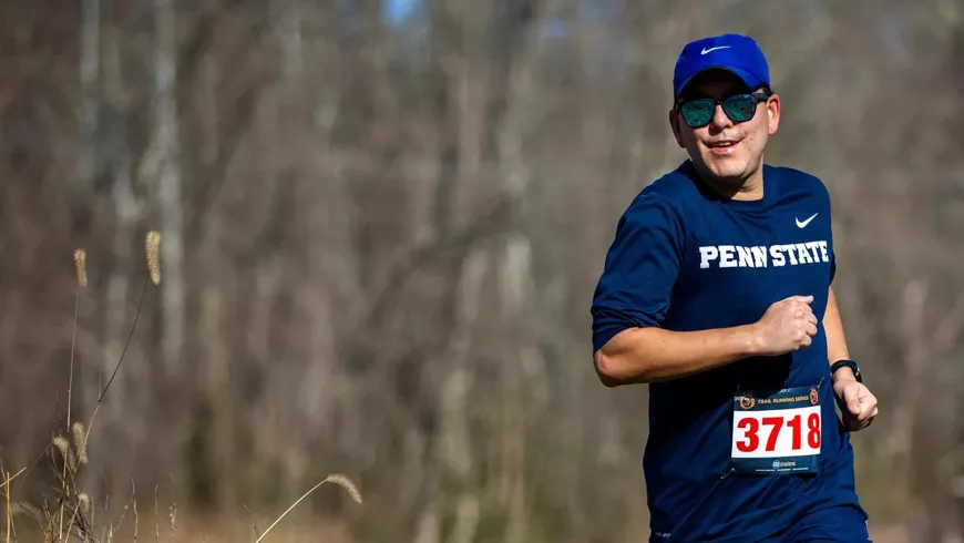 A man wearing a Penn State shirt runs in the woods.