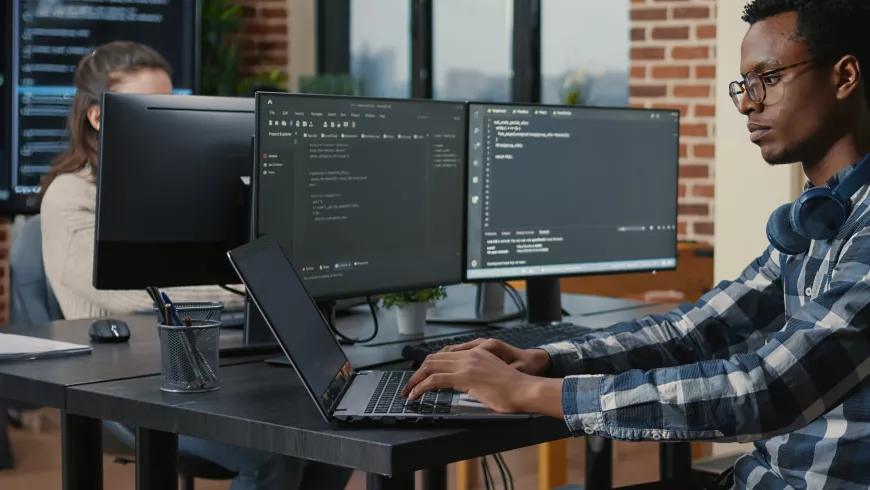 Young man works at a desktop computer with code on the screen.