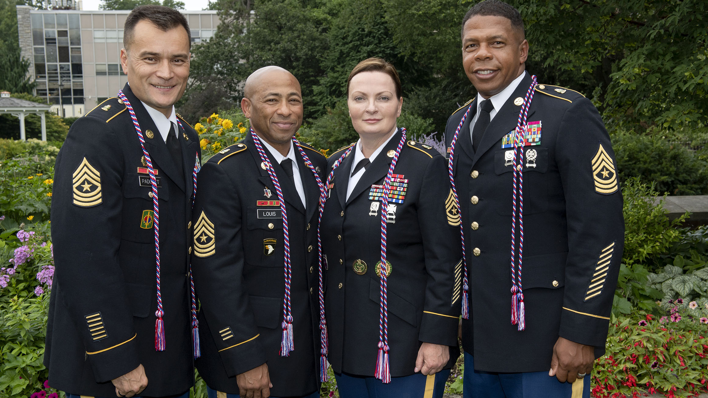 Four soldiers stand in their uniforms with military honor cords around their necks